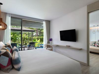 Nowoczesny pokój hotelowy z łóżkiem podwójnym, telewizorem i widokiem na taras z meblami ogrodowymi.