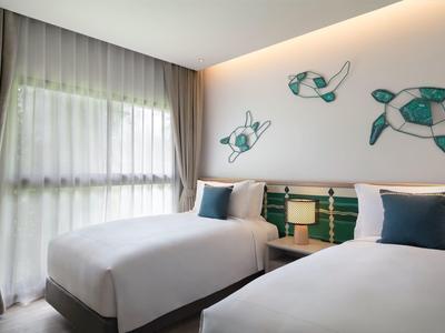 Nowoczesny pokój hotelowy z dwoma łóżkami pojedynczymi, morską dekoracją ściany i naturalnym światłem.