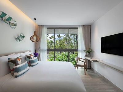 Nowoczesny pokój hotelowy z dużym łóżkiem, telewizorem na ścianie i widokiem na zieloną przyrodę.