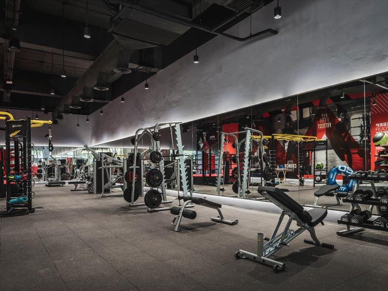 Przestronna siłownia z ciężarami, ławkami i lustrami na ścianie.