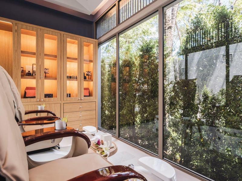Przytulny pokój spa z fotelami do masażu przy dużych oknach z widokiem na zielone rośliny.