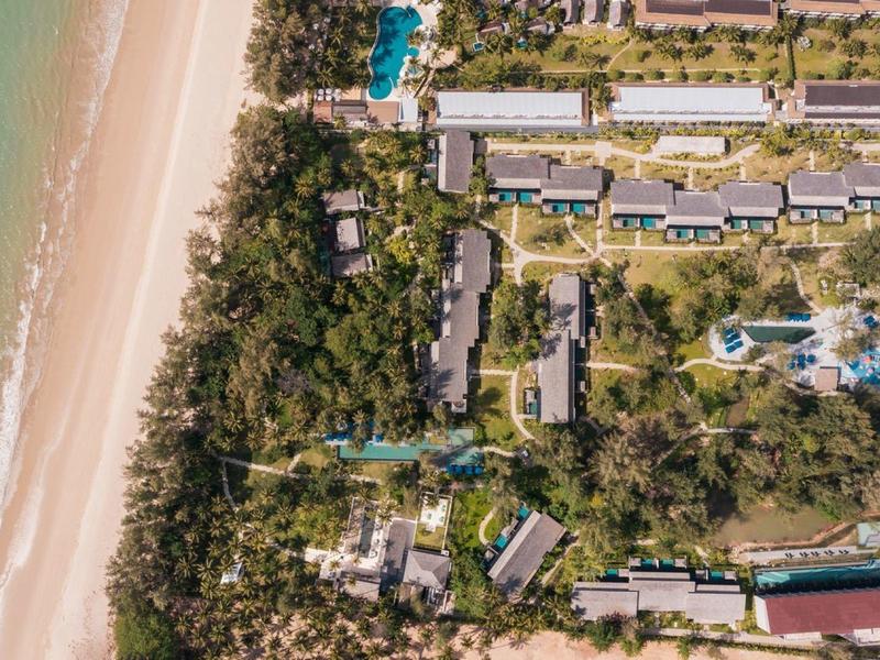 Widok z lotu ptaka ośrodka przy plaży z basenem, zielonymi drzewami i przylegającą piaszczystą plażą.