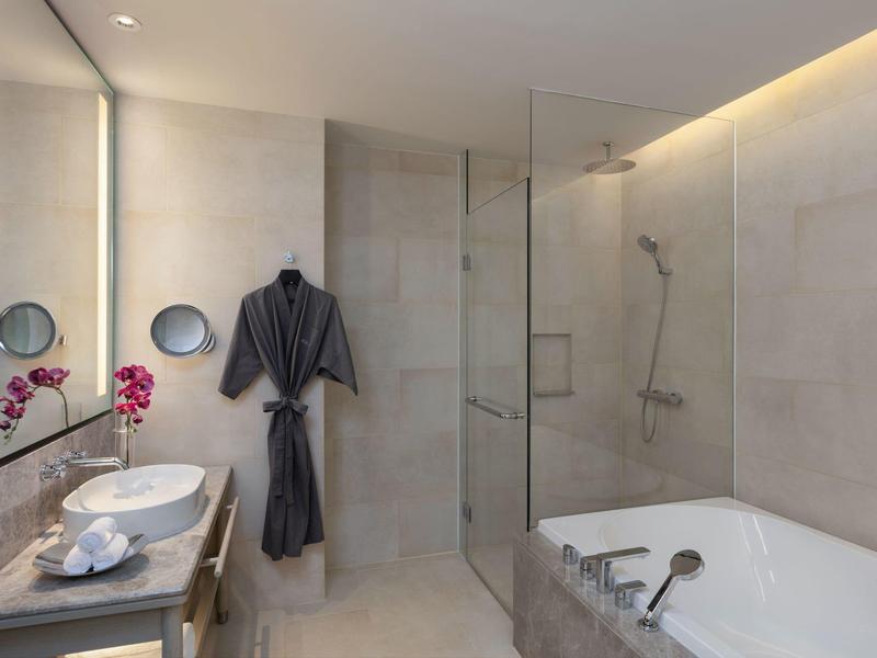 Nowoczesna łazienka z wanną, prysznicem, podwójnymi umywalkami i szarym szlafrokiem.