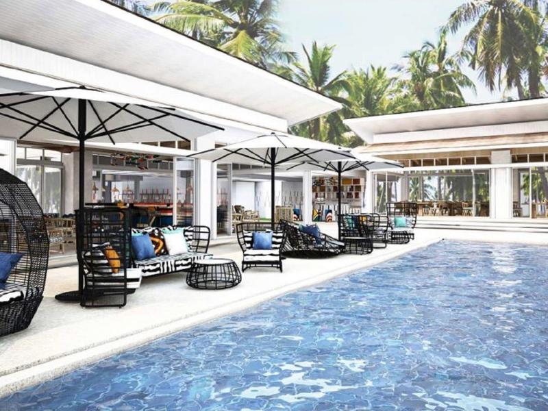 Nowoczesny basen na zewnątrz z leżakami i dużymi parasolami otoczony tropikalną roślinnością.