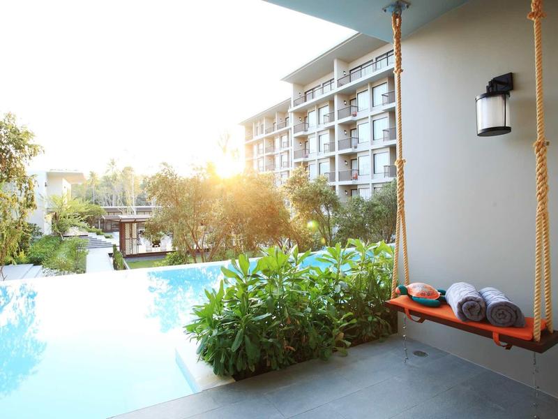 Houpačka s ručníky u bazénu s výhledem na hotelovou budovu za západu slunce.