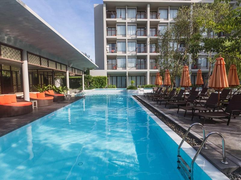 Moderní venkovní bazén s lehátky a slunečníky vedle hotelové budovy