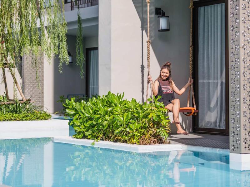 Žena sedí na houpačce vedle bazénu u moderního hotelového pokoje.