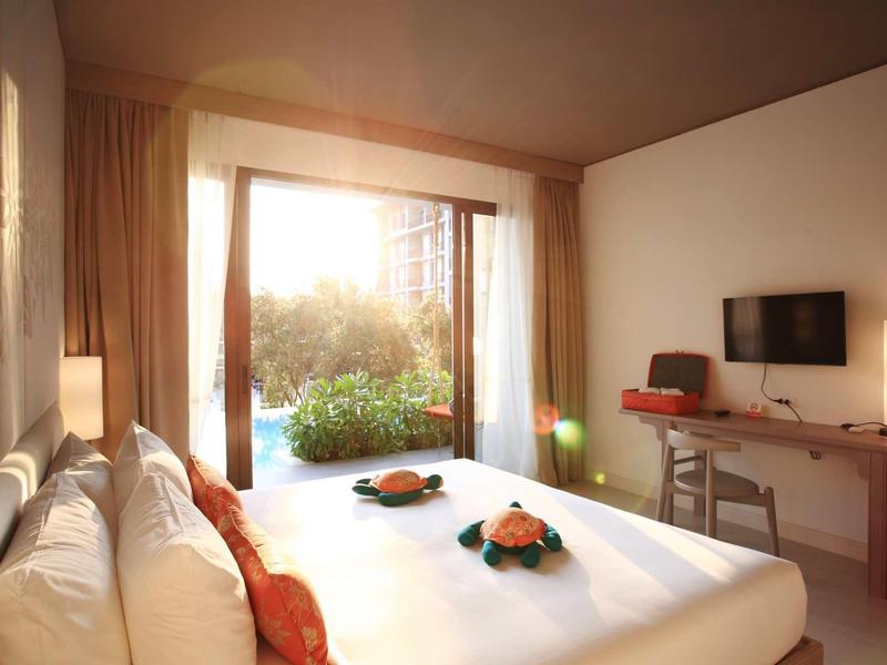 Světelný hotelový pokoj s velkou postelí, TV a terasou s výhledem na zeleň.