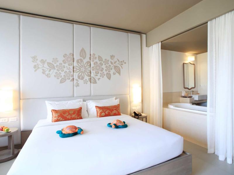 Moderní hotelový pokoj s velkou postelí, elegantní dekorací na zdi a přilehlou koupelnou.