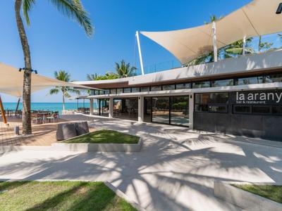 Moderní plážový pavilon se slunečními plachtami a palmami na tropické pláži.