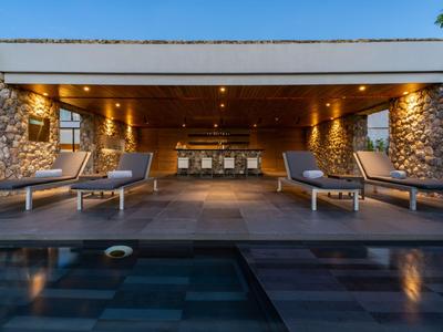 Moderní terasa s bazénem, lehátky a útulnou krytou posezením za soumraku.