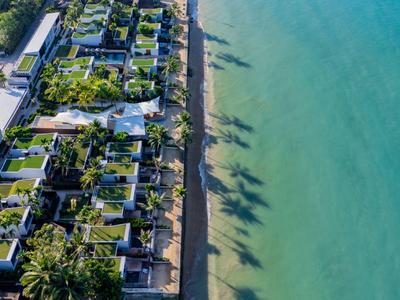 Letecký pohled na hotelový areál s přímým přístupem na tyrkysovou pláž a stíny palem.