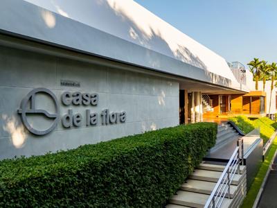 Moderní hotelový vstup se zeleným živým plotem, schody a cedulí 'case de la flore'.