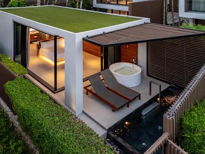 Moderní venkovní prostor s lehátky, vanou a bazénem obklopený zelenými keři