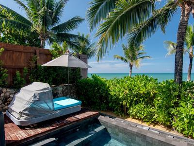 Luxusní bazénová oblast s lehátkem, slunečníkem a výhledem na palmy a oceán.