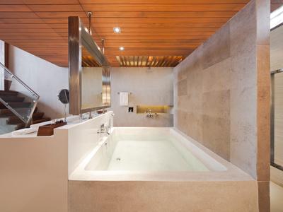Moderní vana v světlé koupelně s dřevěným stropem a schody v pozadí.