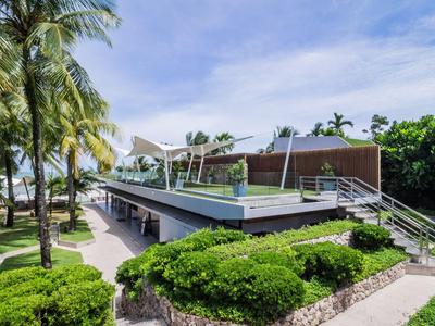 Moderní hotelová budova s bazénem, palmami a upravenou zelení pod modrou oblohou.