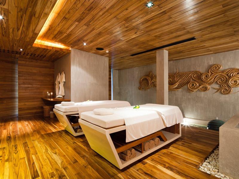 Moderní masážní místnost s dřevěnou podlahou, dřevěnými stěnami a dvěma lehátky s bílými potahy.