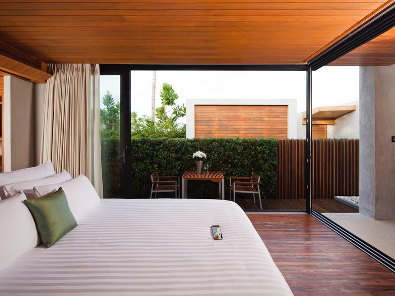 Moderní hotelový pokoj s velkou postelí, dřevěnou podlahou a výhledem na terasu se zahradou