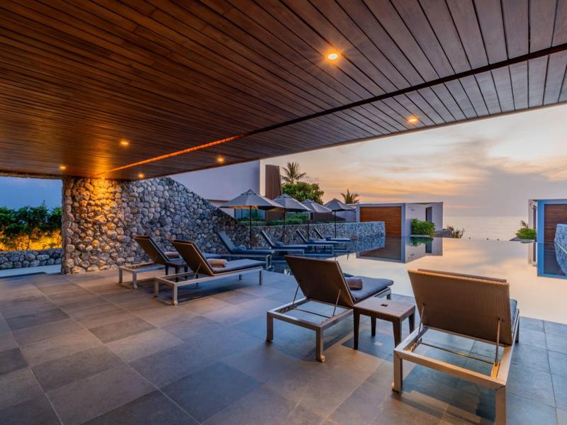 Moderní venkovní terasa s pohodlnými lehátky a výhledem na bazén při západu slunce.