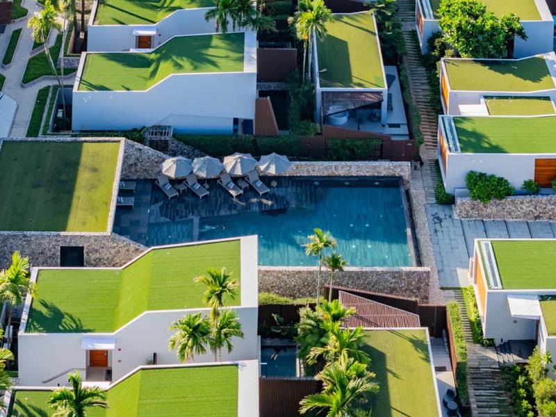 Pohled z ptačí perspektivy na moderní hotelový komplex se zelenými střechami a centrálním bazénem.