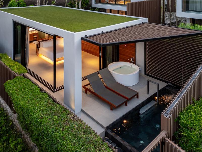 Moderní hotelový bungalov se skleněnými stěnami, vířivkou, lehátky a malým rybníčkem venku.