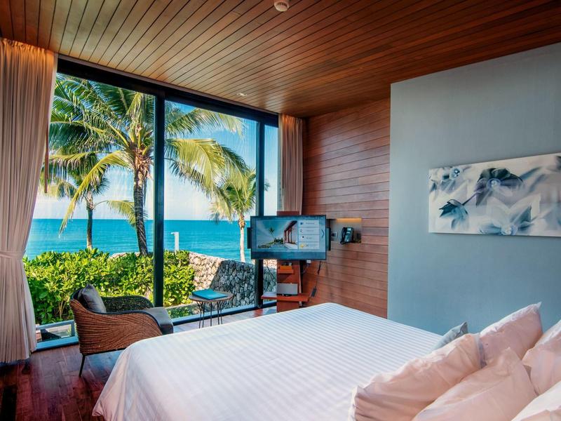 Moderní hotelový pokoj s výhledem na moře, velkými okny a tropickým prostředím.