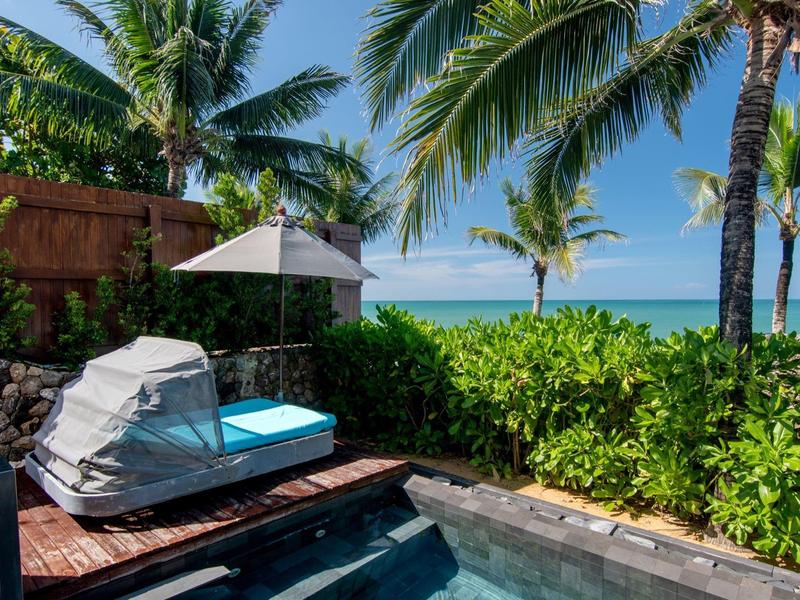 Luxusní bazénová oblast s lehátkem, slunečníkem a výhledem na palmy a oceán.