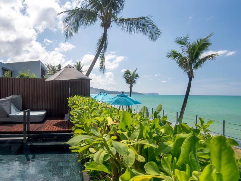 Pohled na tropické rostliny, palmy a modré moře z hotelové terasy u pláže.