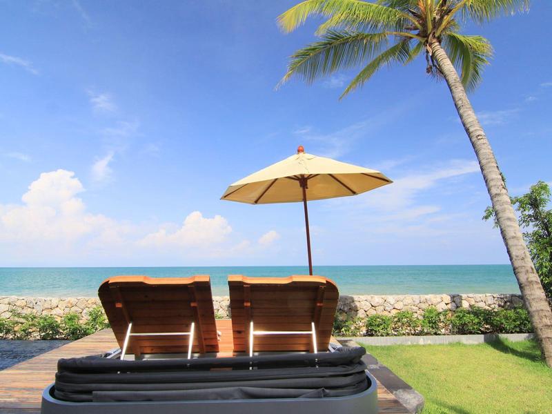 Dva lehátka pod slunečníkem u palm s výhledem na moře