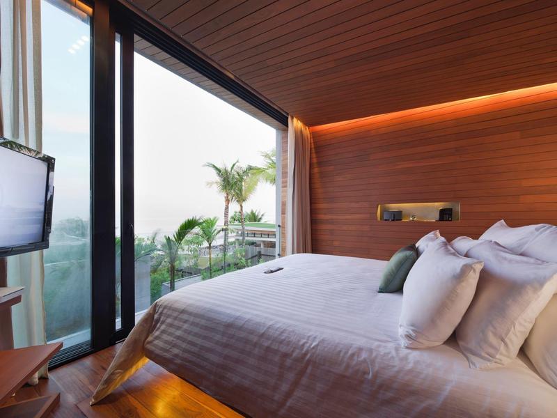 Moderní hotelový pokoj s velkou postelí a balkonem s výhledem na palmy.