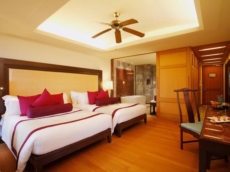 Jasny pokój hotelowy z dwoma łóżkami, drewnianą podłogą, wentylatorem sufitowym i biurkiem z krzesłem.