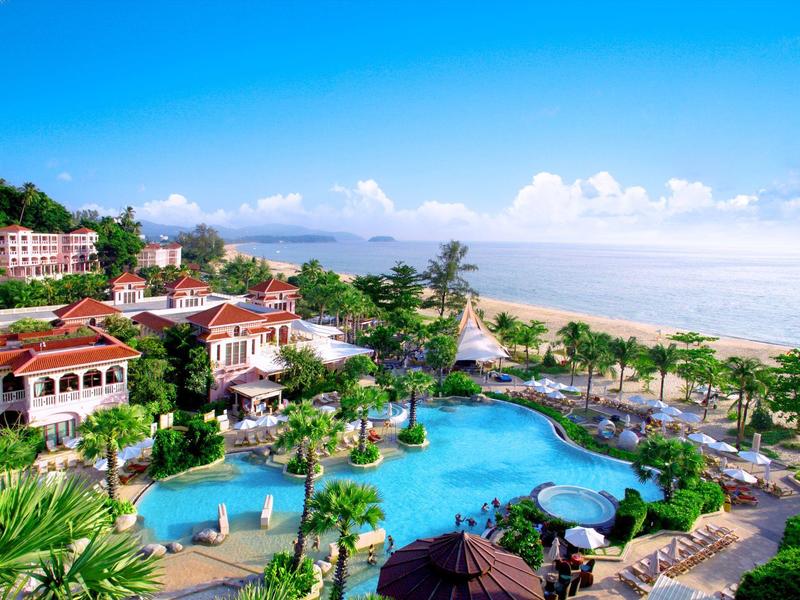 Ośrodek z dużym basenem, palmami i plażą z spokojnym morzem pod niebieskim niebem.