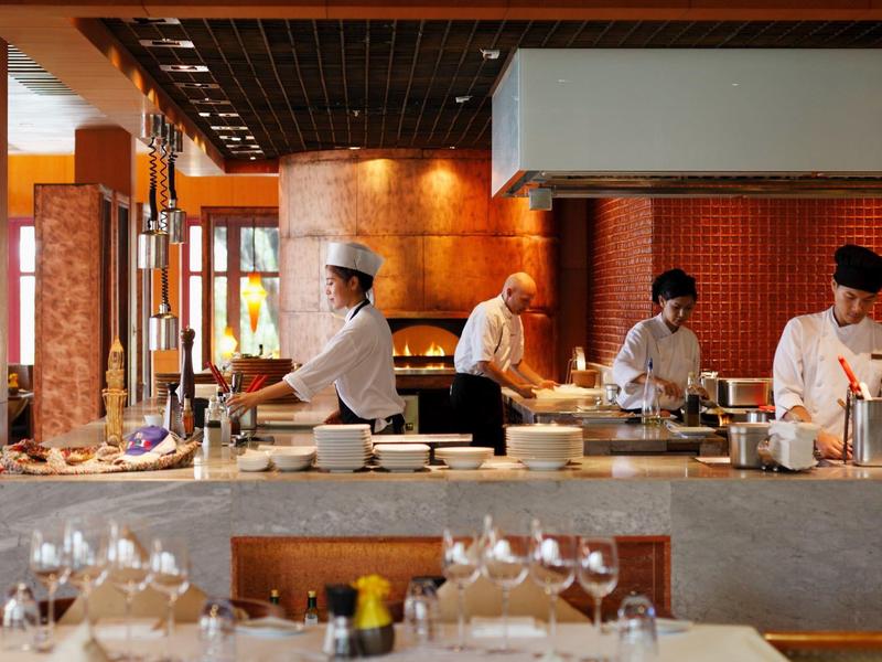 Kucharze przygotowują jedzenie w nowoczesnej kuchni restauracyjnej z nakrytymi stołami na pierwszym planie.