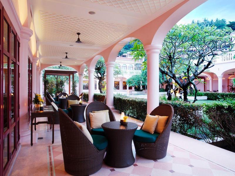 Zewnętrzny teren wypoczynkowy z poduszkowanymi krzesłami i stolikami przy arkadowej werandzie obok ogrodu.