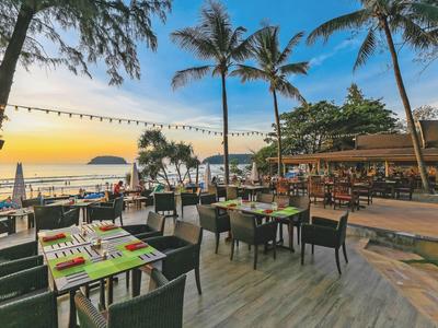 Offenes Strandrestaurant mit Tischen und Stühlen, Palmen und Sonnenuntergang am Meer.