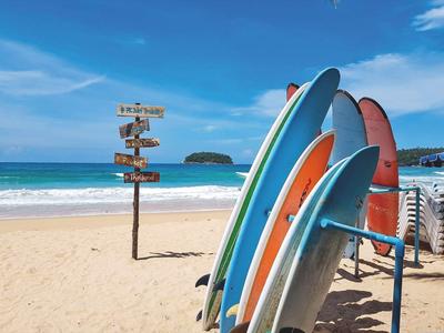 Strand mit mehreren bunten Surfbrettern auf Sand und Wegweiser vor blauem Himmel und Meer.