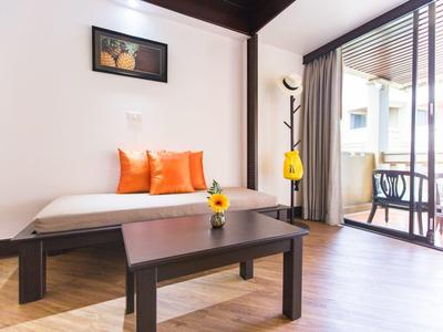 Helles Wohnzimmer mit Tagesbett, orangefarbenen Kissen, Holztisch und Balkon mit Stühlen und Tisch.