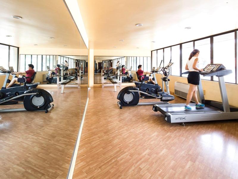 Moderner Fitnessraum mit Laufband, Fahrradergometern, Holzfußboden und großen Fenstern.