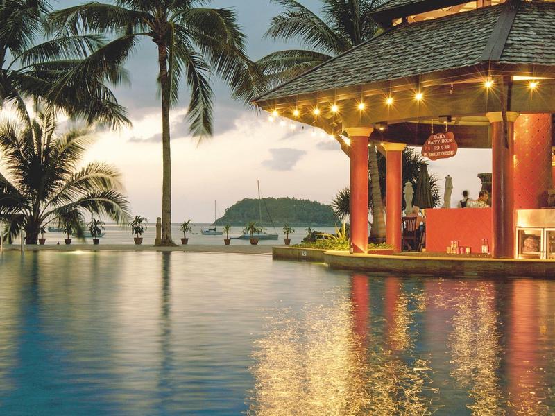 Ein beleuchteter Poolbar mit Palmen und Meerblick bei Sonnenuntergang.