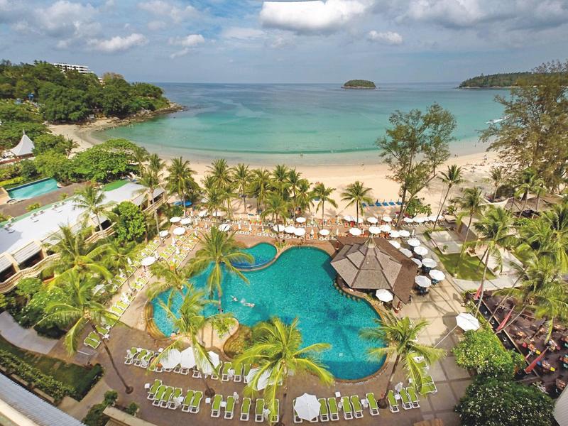 Blick auf tropischen Sandstrand mit Palmen, Pools und Sonnenschirmen unter blauem Himmel.