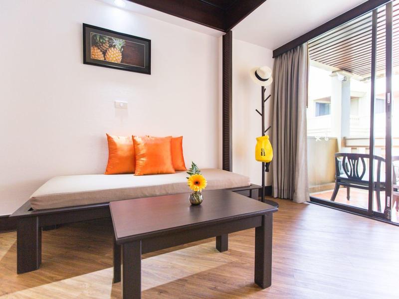 Helles Wohnzimmer mit Tagesbett, orangefarbenen Kissen, Holztisch und Balkon mit Stühlen und Tisch.