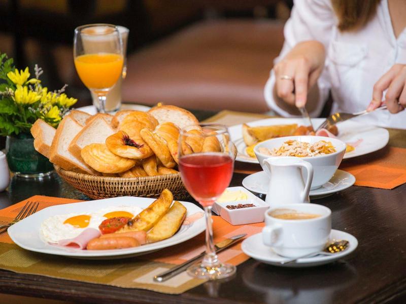 Frühstückstisch mit Brötchen, Orangensaft, Tee, Marmelade und einer Person beim Essen.