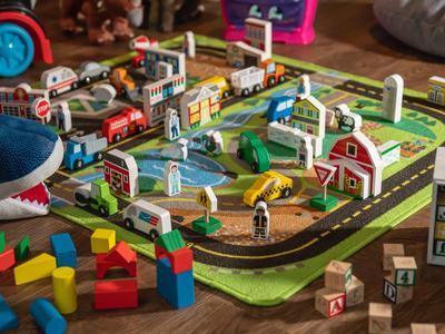 Bunter Holzeisenbahn-Spielplatz mit Häusern und Fahrzeugen auf einem Teppich.