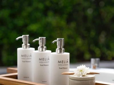 Tres botellas blancas con bomba y una pequeña maceta con flor sobre una bandeja de madera en el baño.