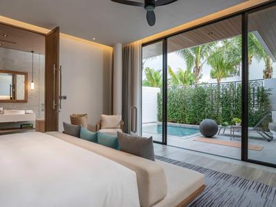 Habitación de hotel moderna con cama grande y vista a una terraza con tumbonas y plantas tropicales.