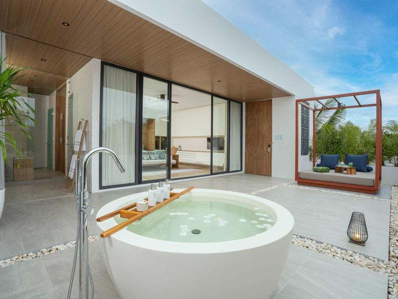 Área exterior moderna con jacuzzi redondo y zona de descanso con cama con dosel bajo el cielo azul.