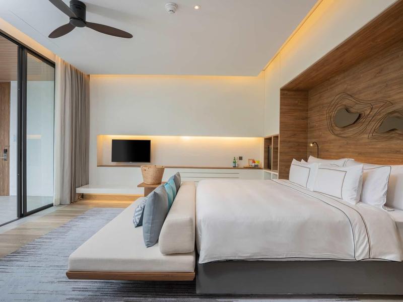 Habitación de hotel moderna con cama grande, banco lateral y fachada de vidrio a la veranda.