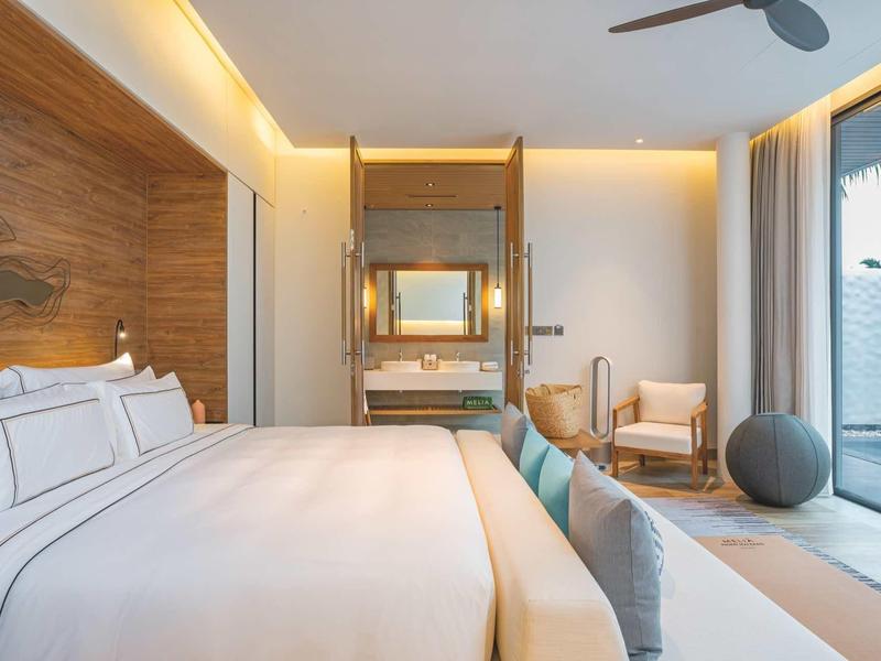 Habitación de hotel luminosa con cama grande, acentos de madera y acceso a terraza con vista al mar.