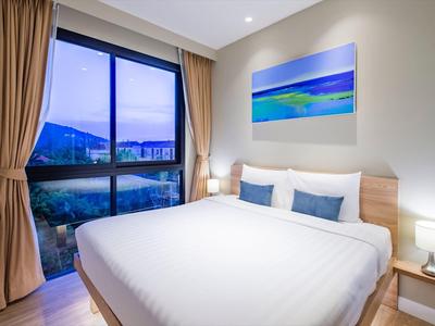 Helles Schlafzimmer mit großem Fenster, weißem Bett, blauen Kissen und blau-grünem Wandbild.